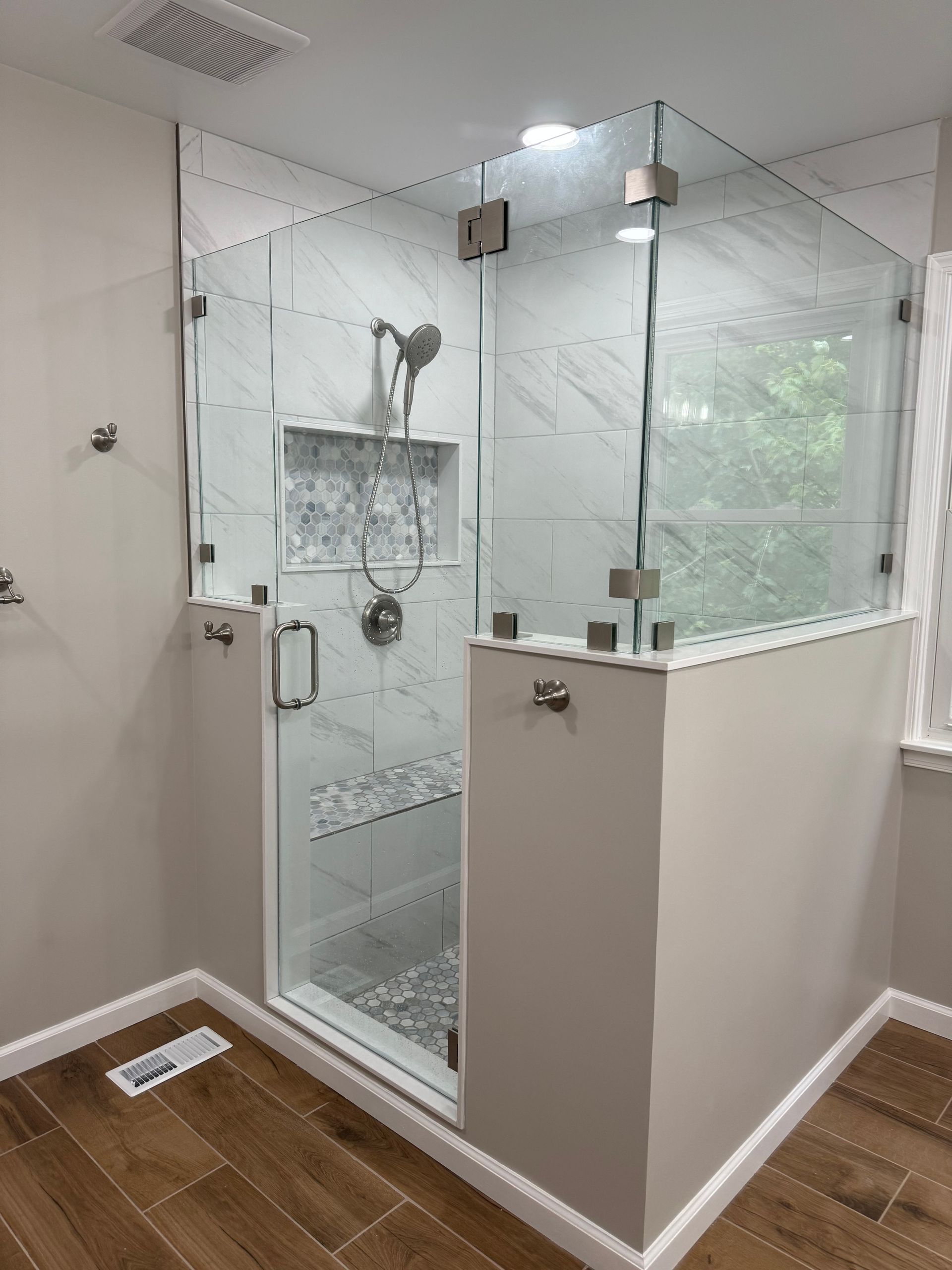 Modern bathroom with glass-enclosed shower, marble tiles, and wood-look flooring.