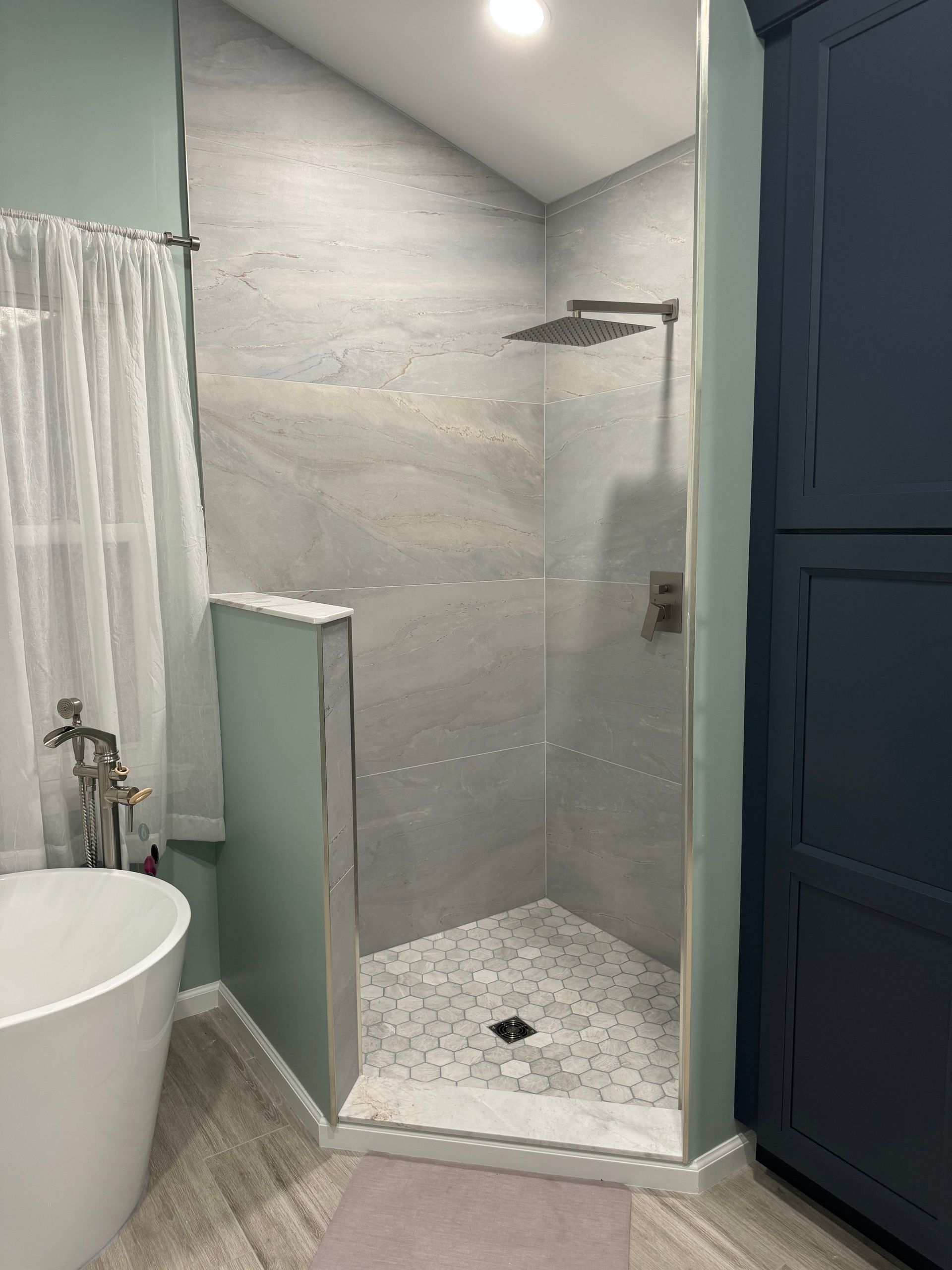 Bathroom shower stall with gray tile, white shower pan, and dark blue cabinets beside it
