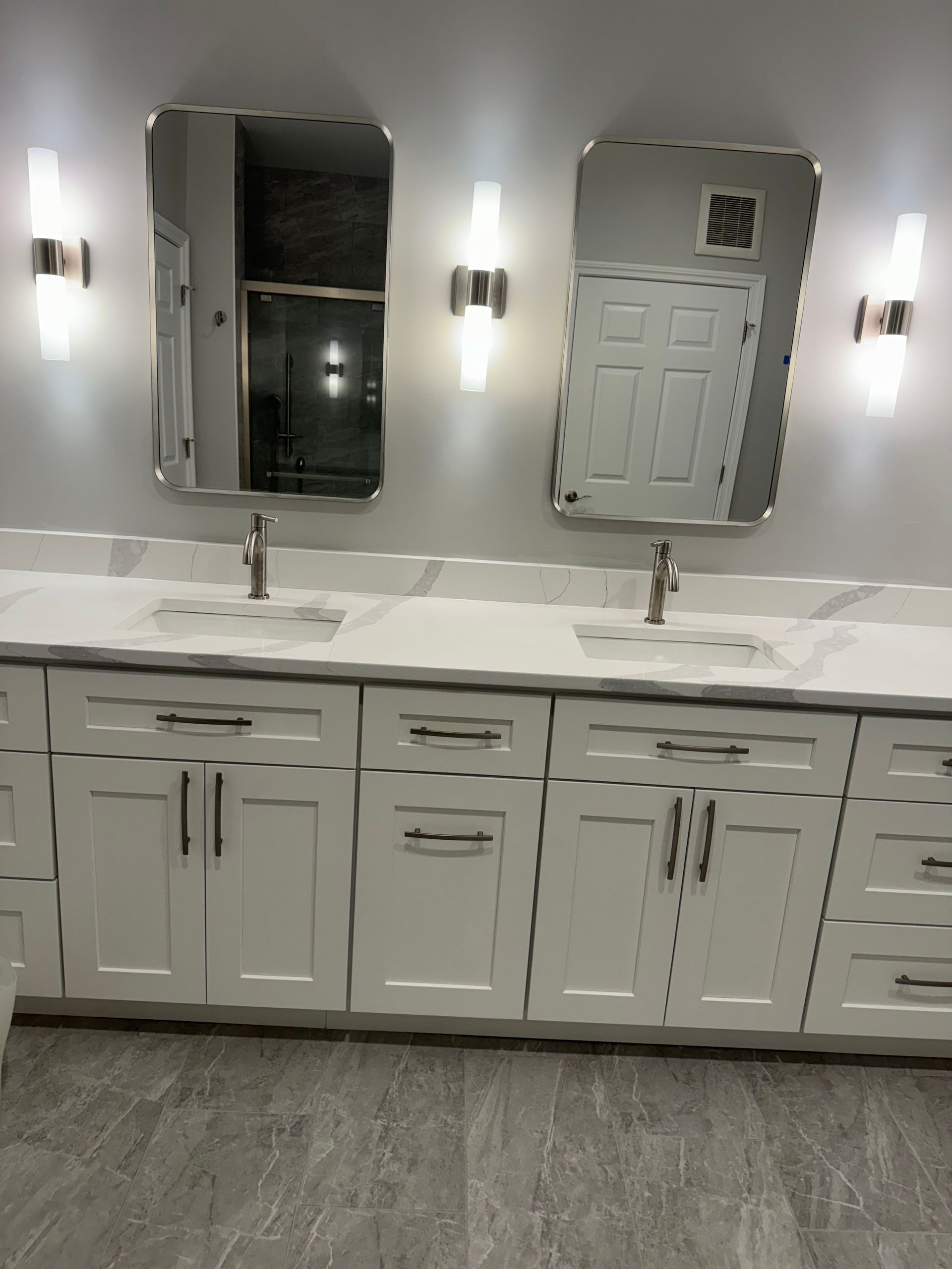 White bathroom vanity with double sinks, mirrors, sconces, and gray tile floor