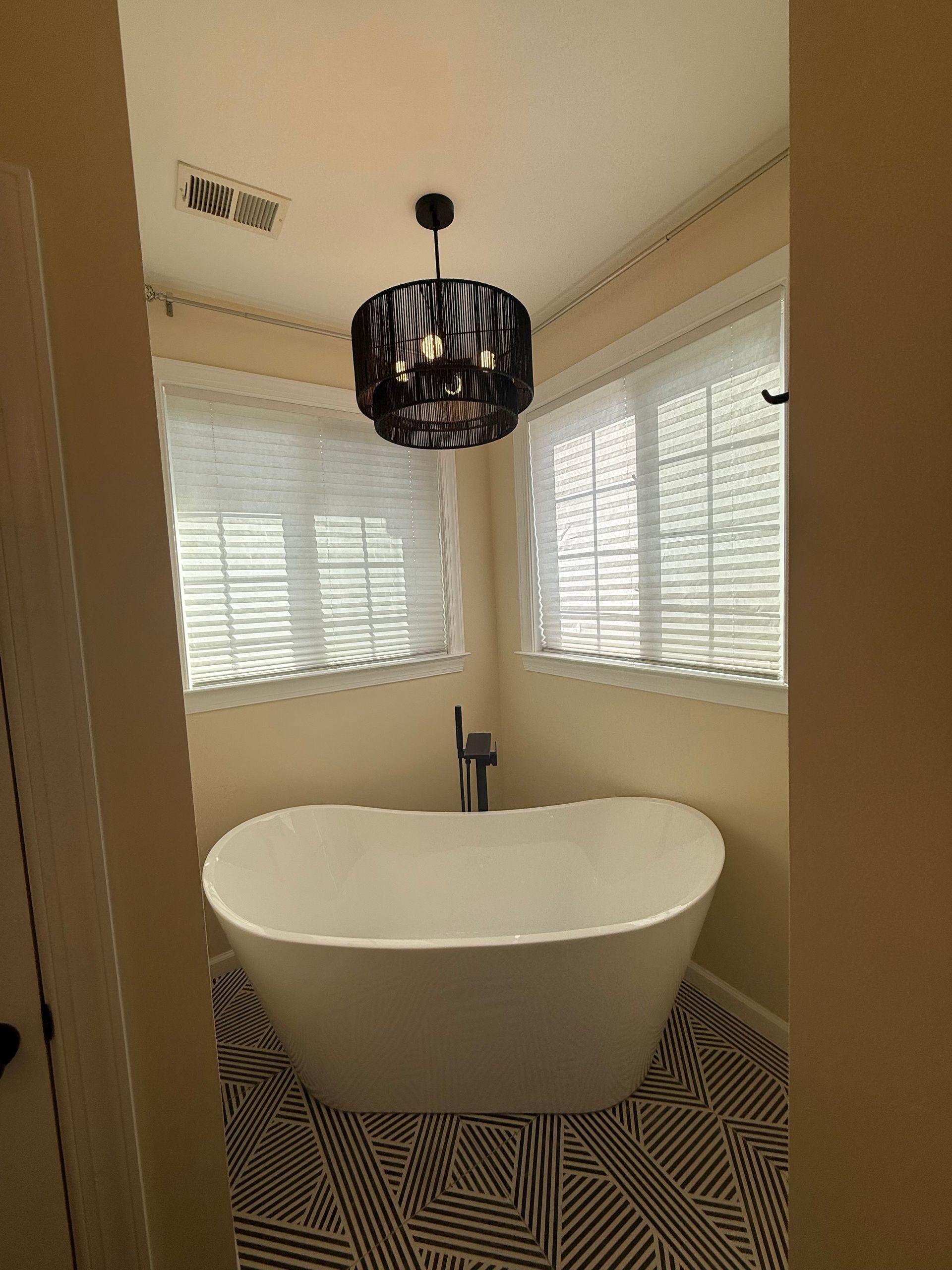 Modern bathroom with a freestanding tub, black chandelier, and white shutters over the windows