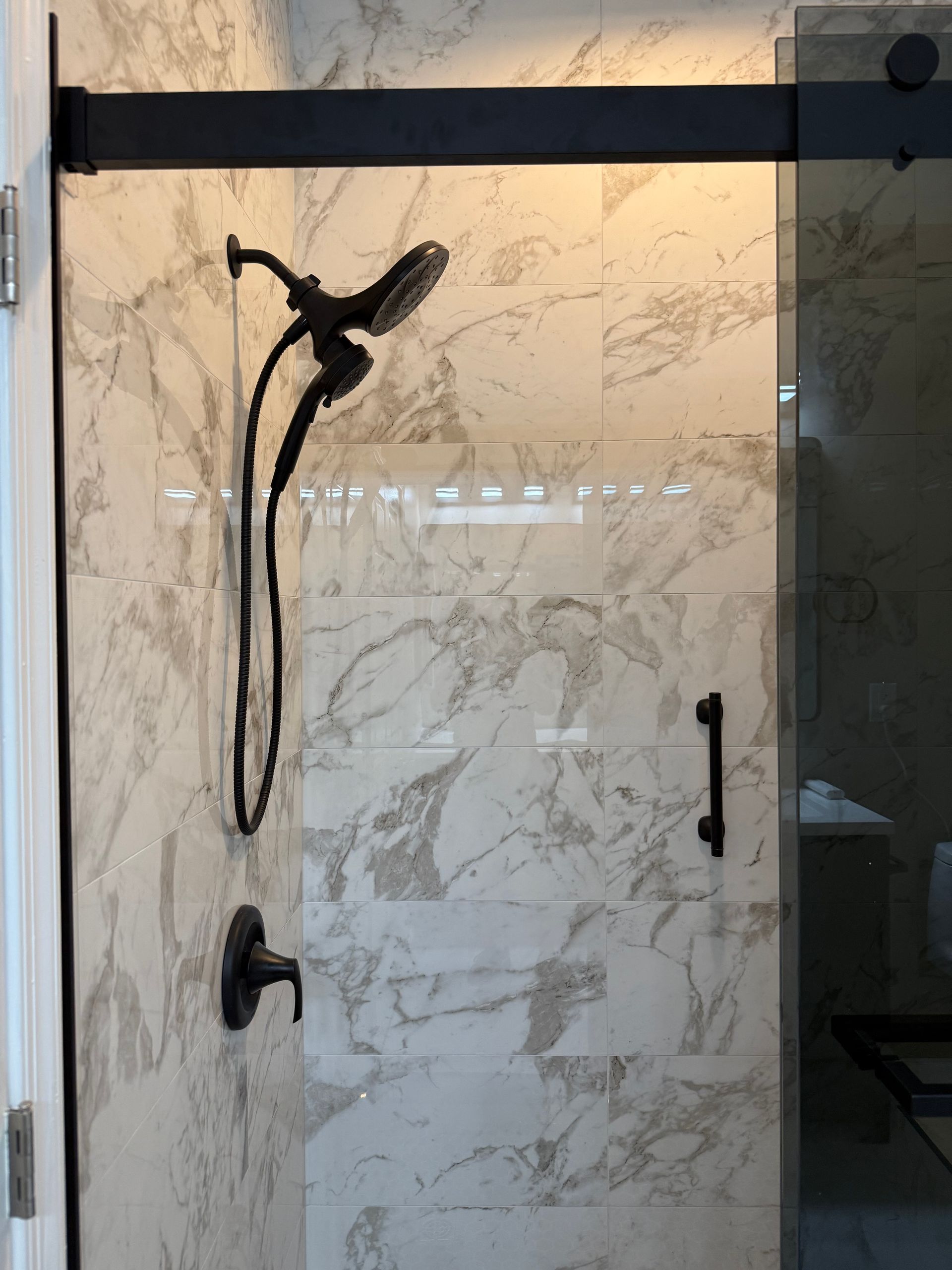 Glass shower enclosure with black hardware and marble-pattern wall tiles