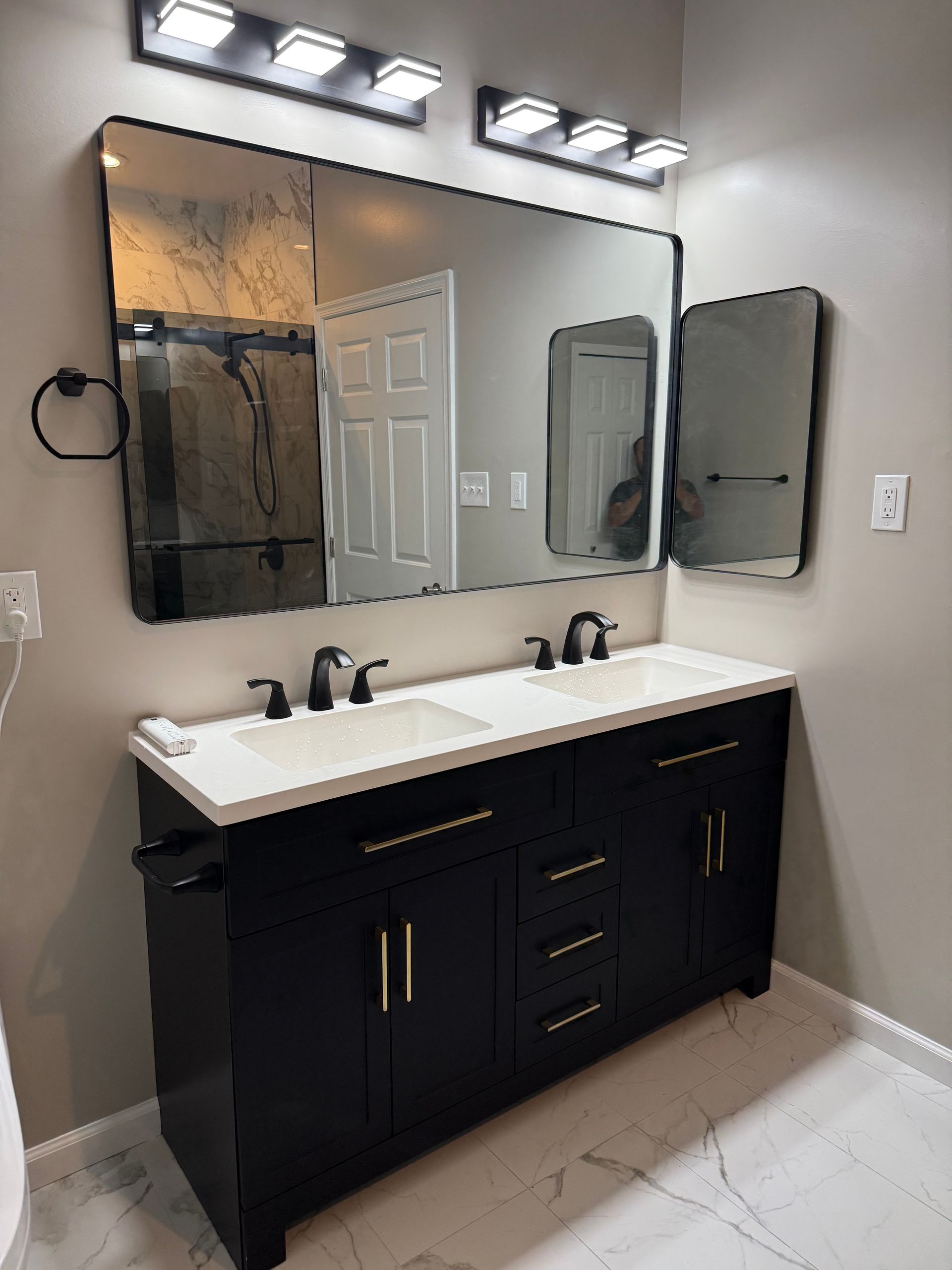 Modern bathroom vanity with two black mirrors, white countertop, and black double sink under vanity lights
