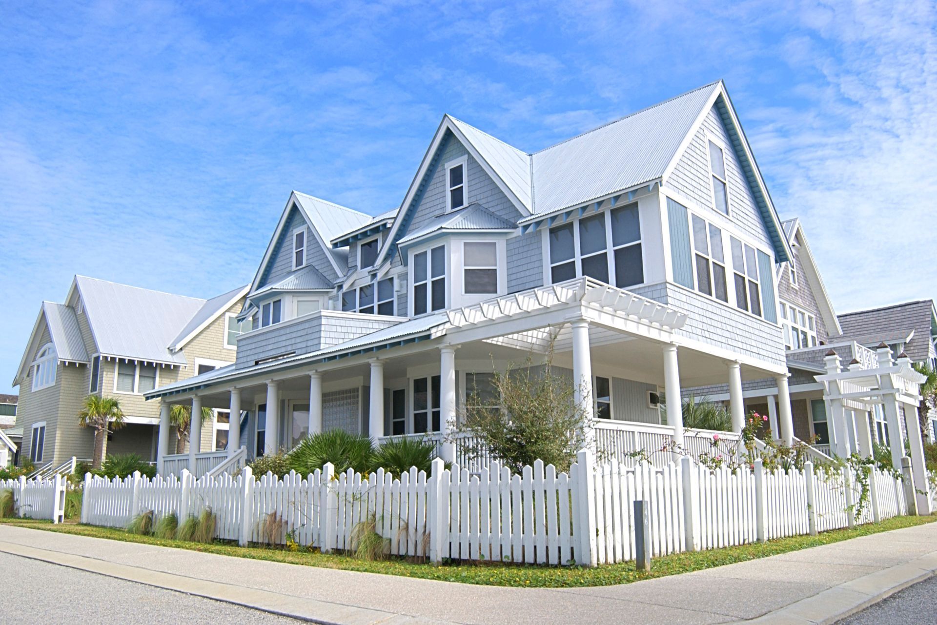 White Victorian-style house with blue roof and white picket fence on a sunny street corner