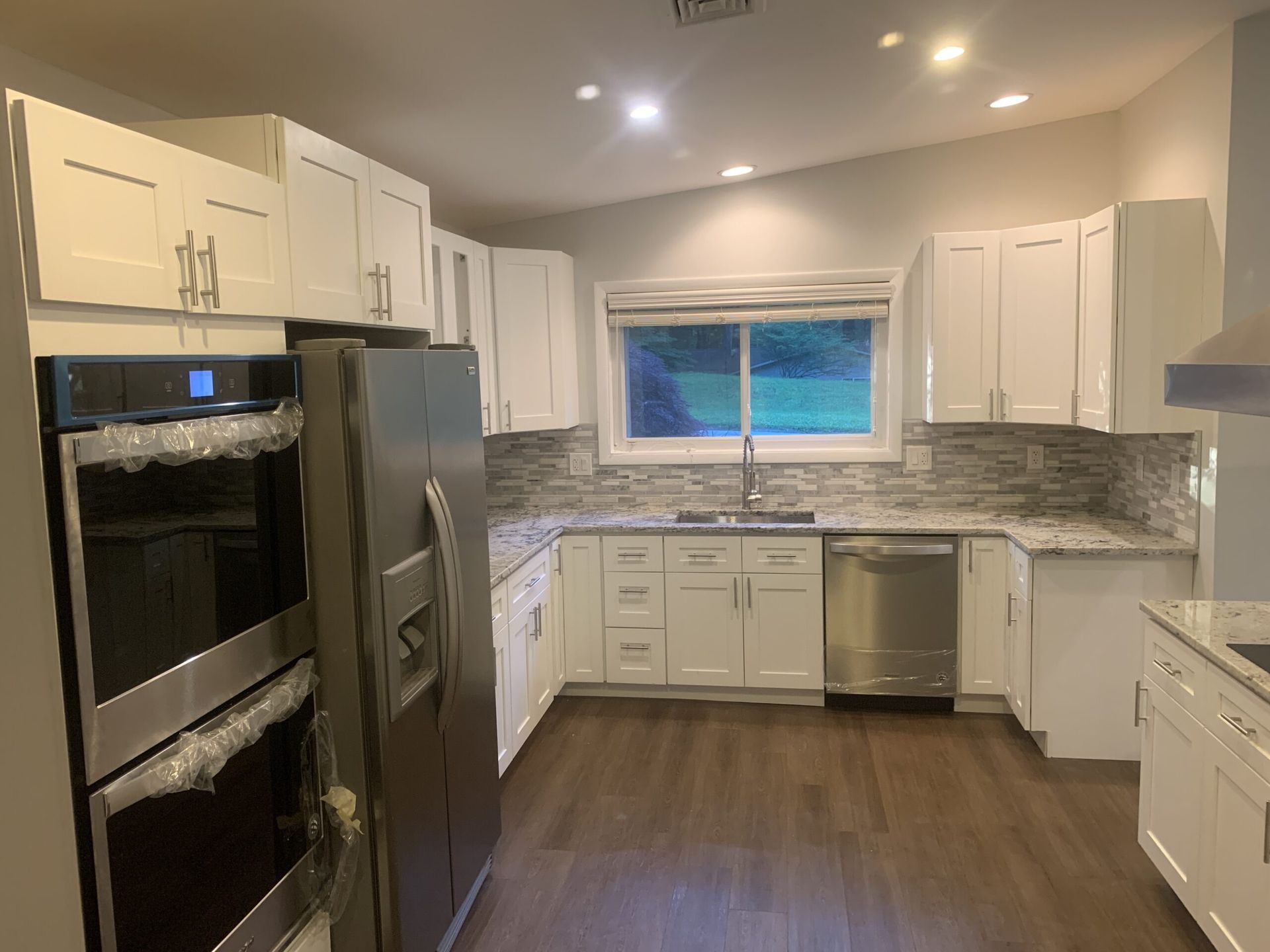 Bright modern kitchen with white cabinets, stainless appliances, and a large window over the sink
