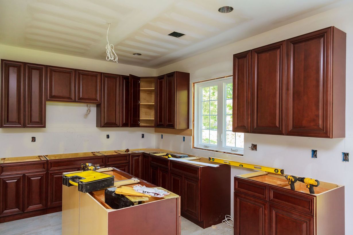 Kitchen under renovation with dark wood cabinets, exposed countertops, and a window above the sink