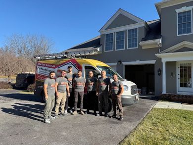 Workers standing in front of a house beside a service van with open rear doors.
