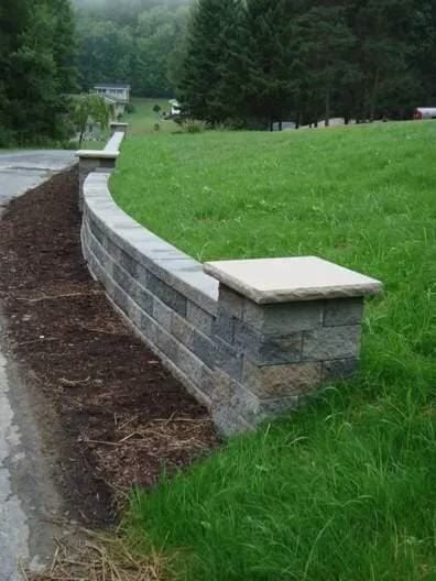 A brick wall is surrounded by grass and dirt next to a road.