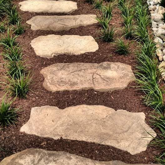 A stone walkway surrounded by grass and rocks in a garden.