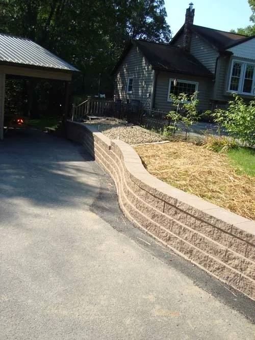 A driveway with a stone wall and a house in the background.