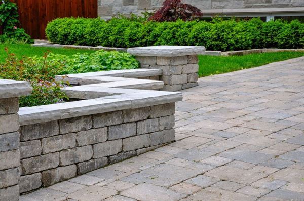 A brick walkway with a stone wall and benches in a backyard.