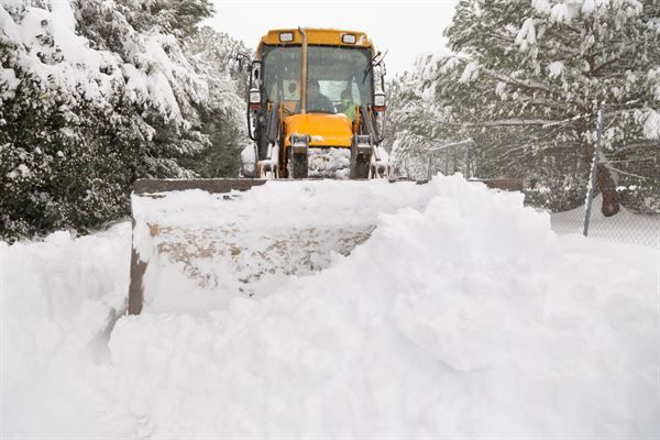 A yellow snow plow is clearing snow from a driveway.