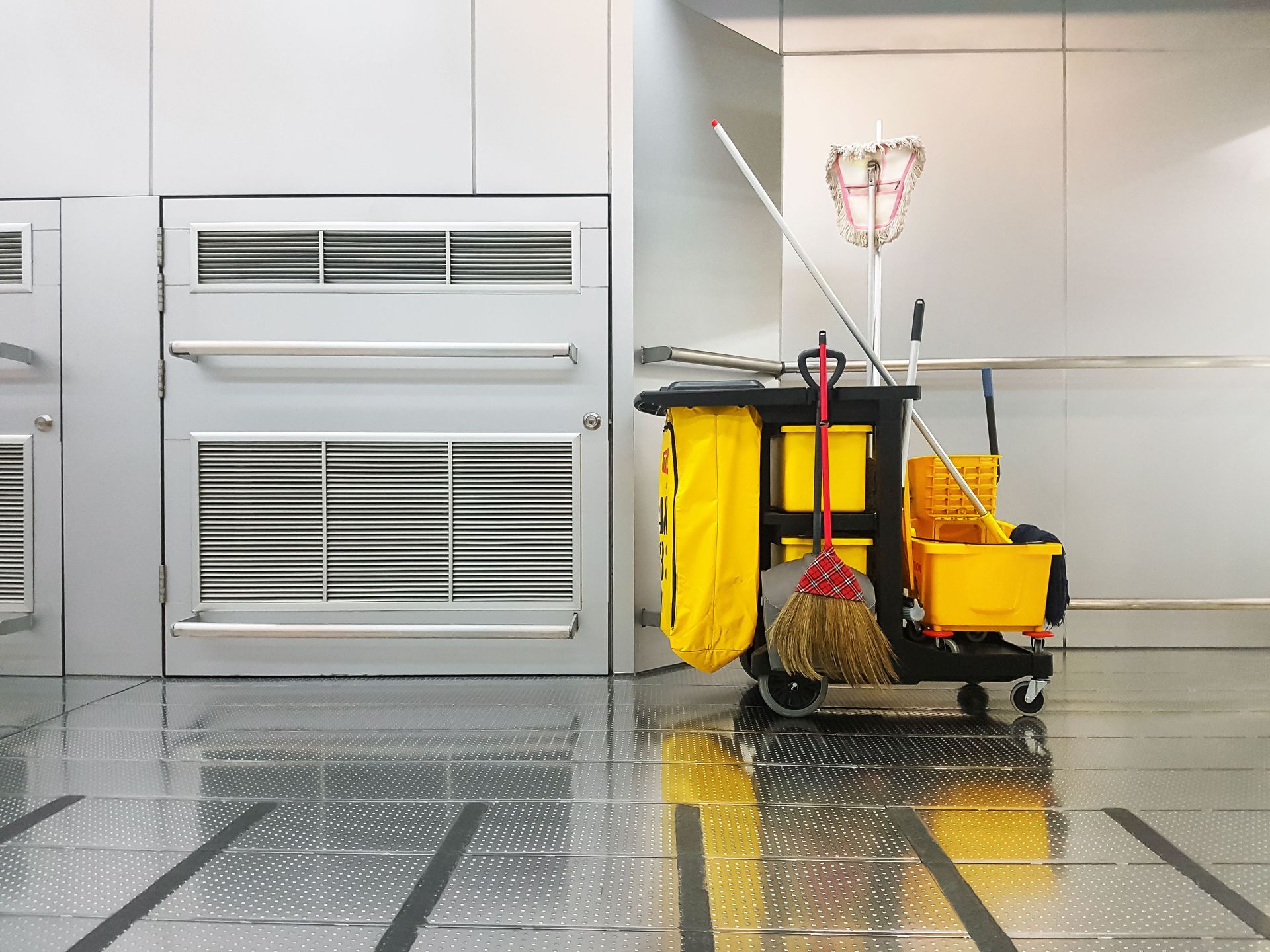 A cleaning cart with a mop , broom and bucket in a kitchen.
