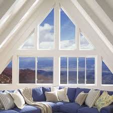 Blue couch beneath large windows in a white-walled attic, showcasing a scenic view of sky and mountains.