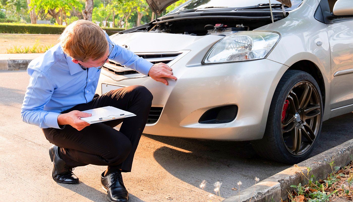 A man is kneeling down in front of a silver car.