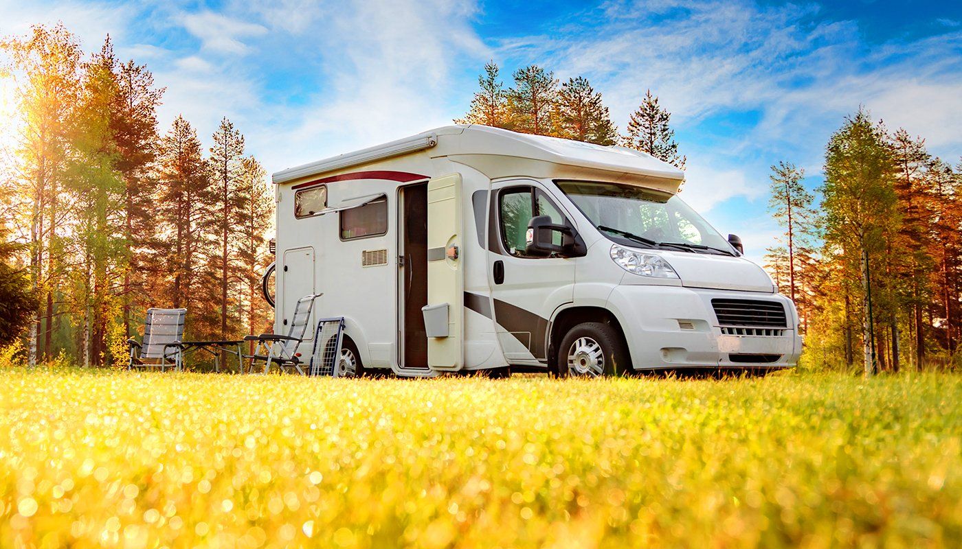 Learn More About RV Insurance A white rv is parked in a field with trees in the background