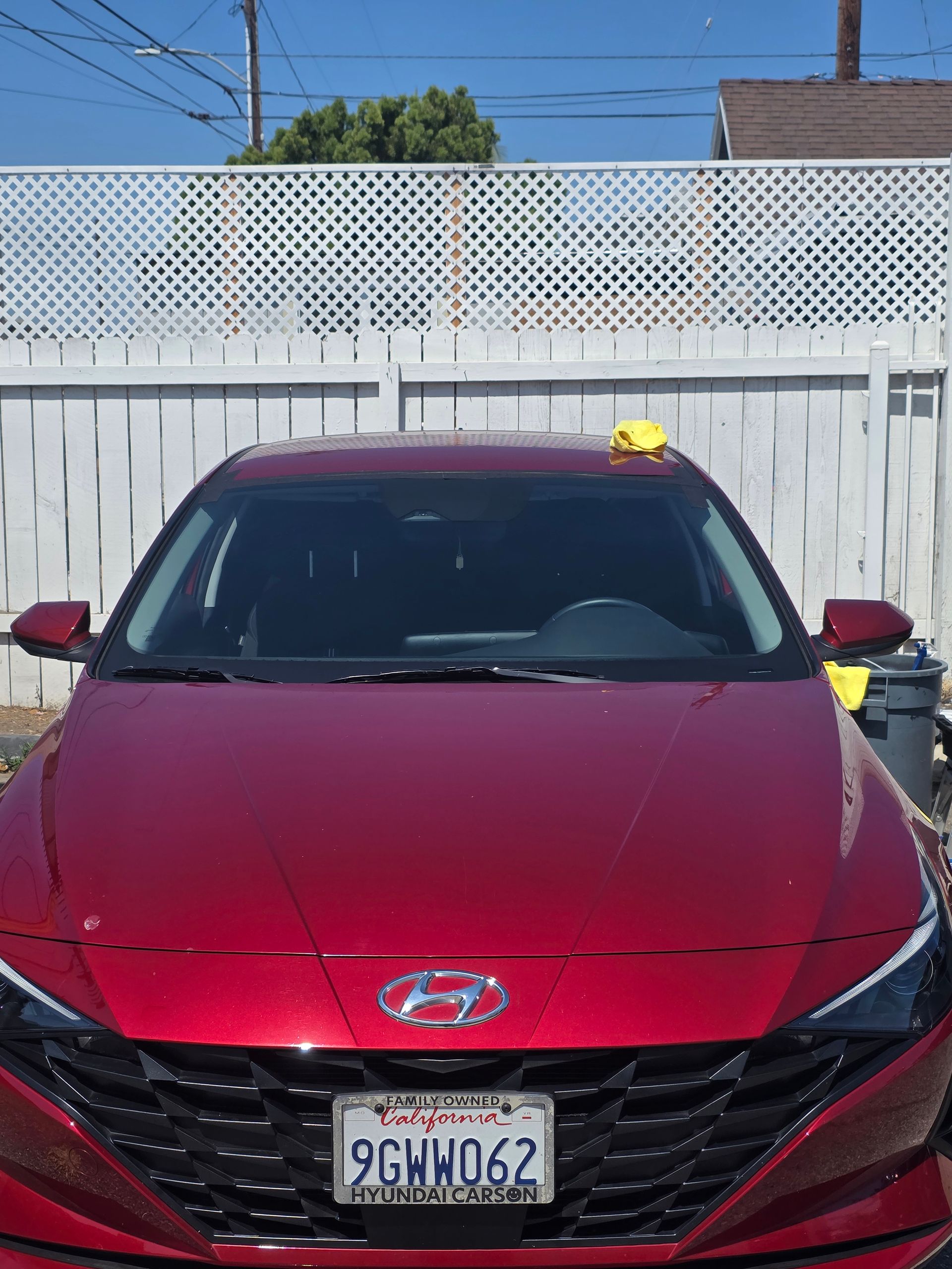 A red Hyundai sedan parked in front of a white picket fence, against a blue sky.