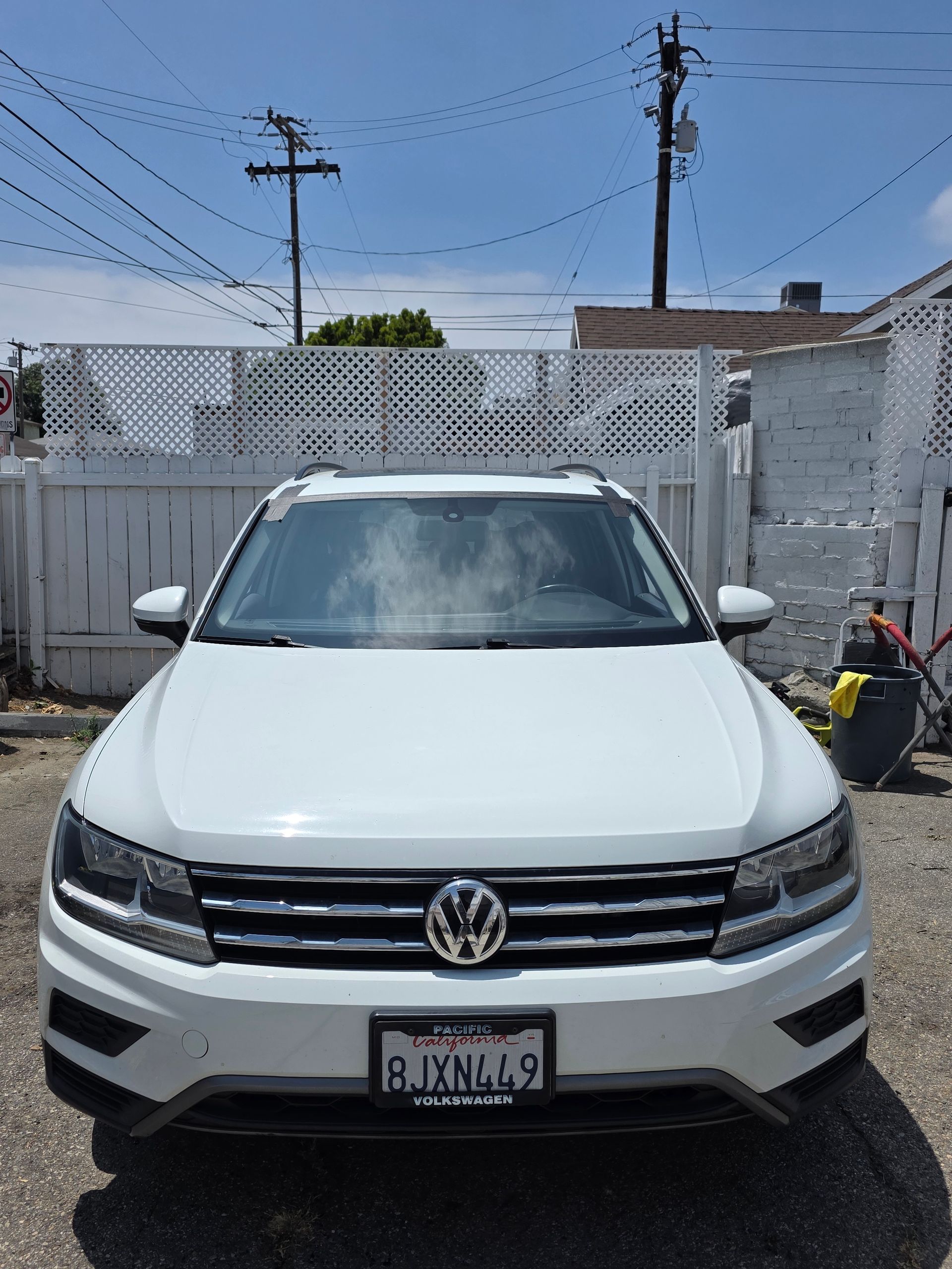 White Volkswagen SUV parked in front of a white fence under a bright blue sky. California license plate.
