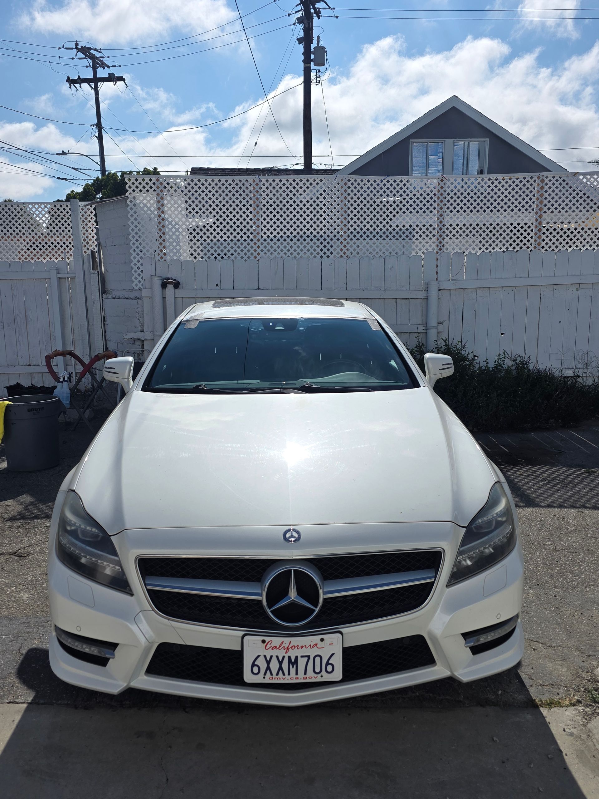 White Mercedes-Benz sedan parked in front of a white fence and house, California license plate visible.