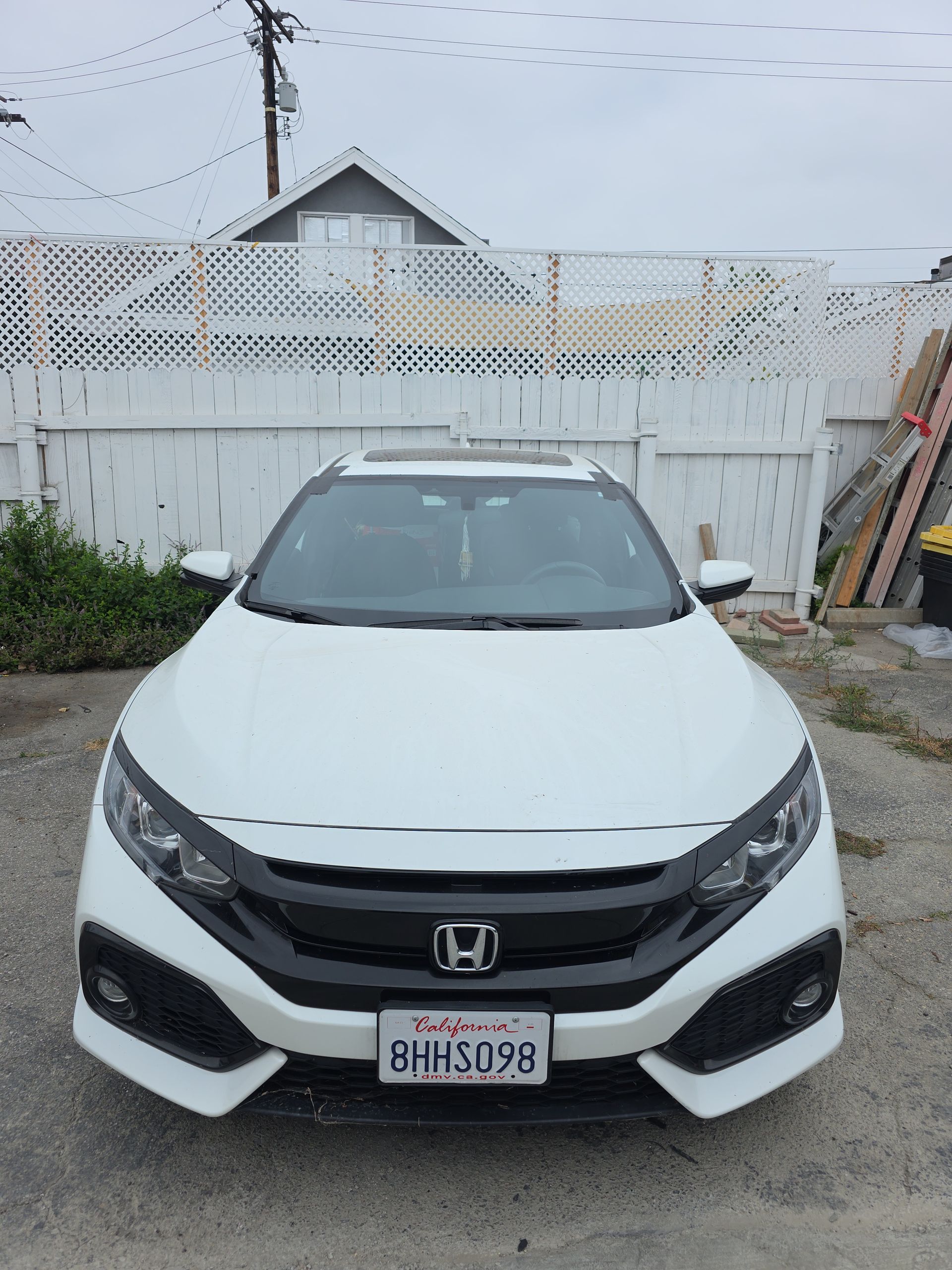 White Honda Civic parked in front of a white fence and a building, with overcast skies.