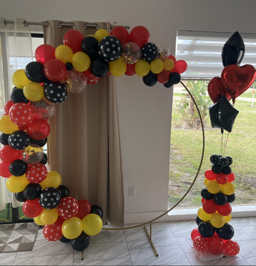 A Mickey Mouse-themed balloon arch with red, black, and yellow balloons, and a matching balloon tower and bouquet