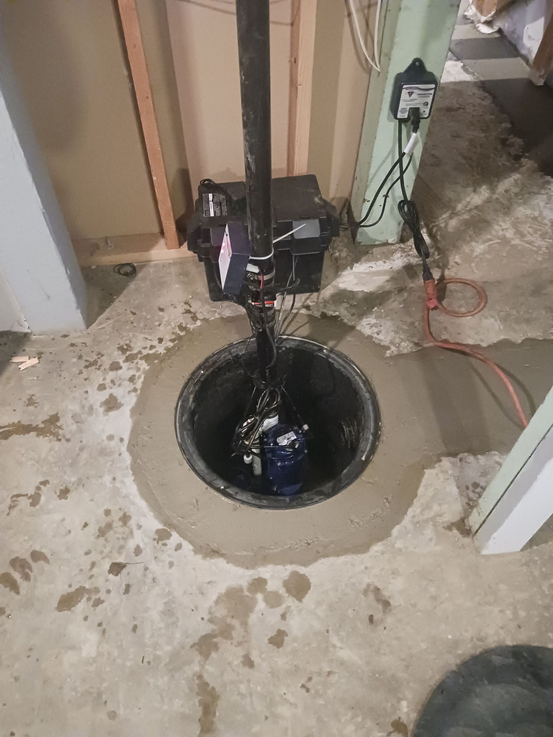 A sump pump is sitting in a hole in the floor of a basement
