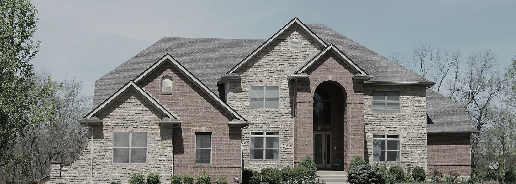 Large two-story house with brick and stone facade under a grey sky.