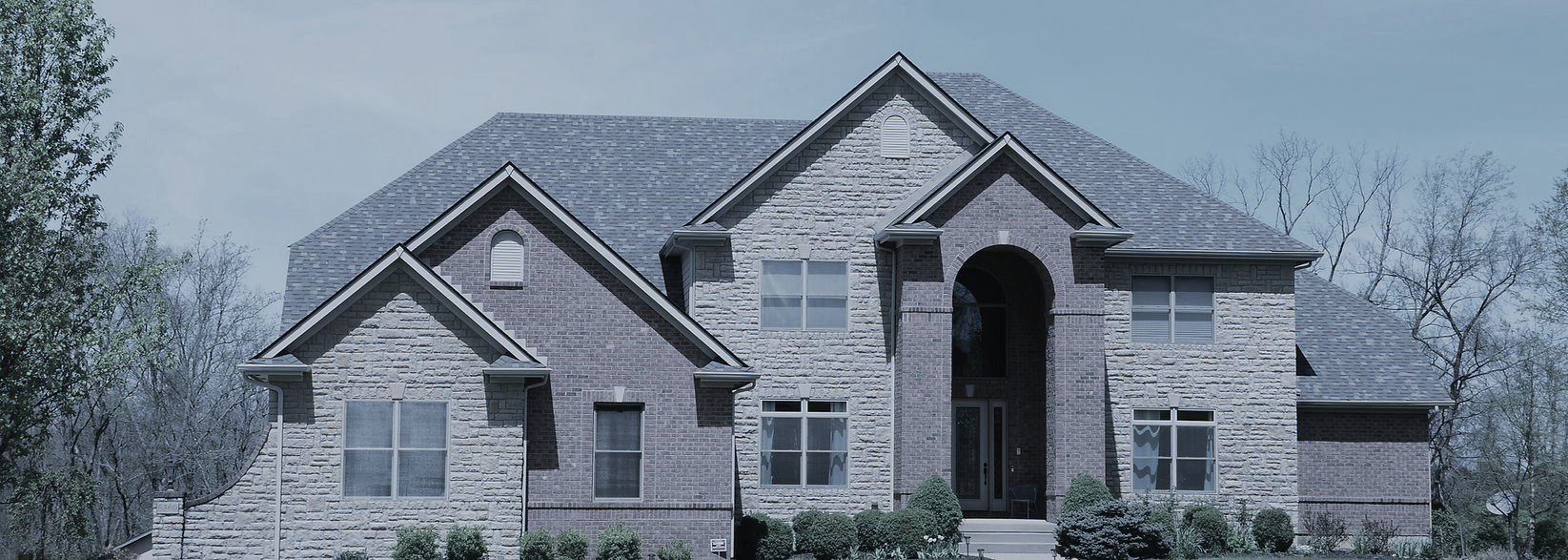 Large two-story house with brick and stone facade under a grey sky.
