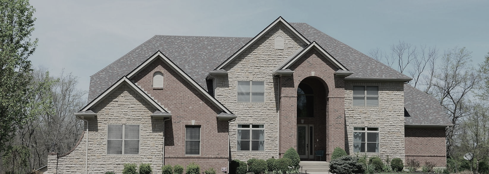 Large two-story house with brick and stone facade under a grey sky.