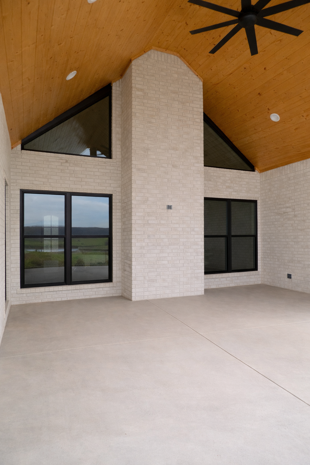 Modern patio with brick accent, large windows, wood ceiling, and a black ceiling fan.