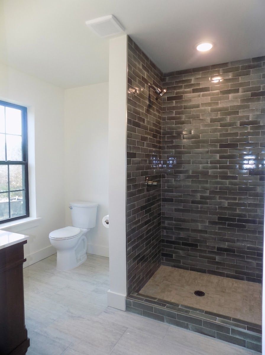 Bathroom with a dark tile shower, white toilet, and wooden vanity.