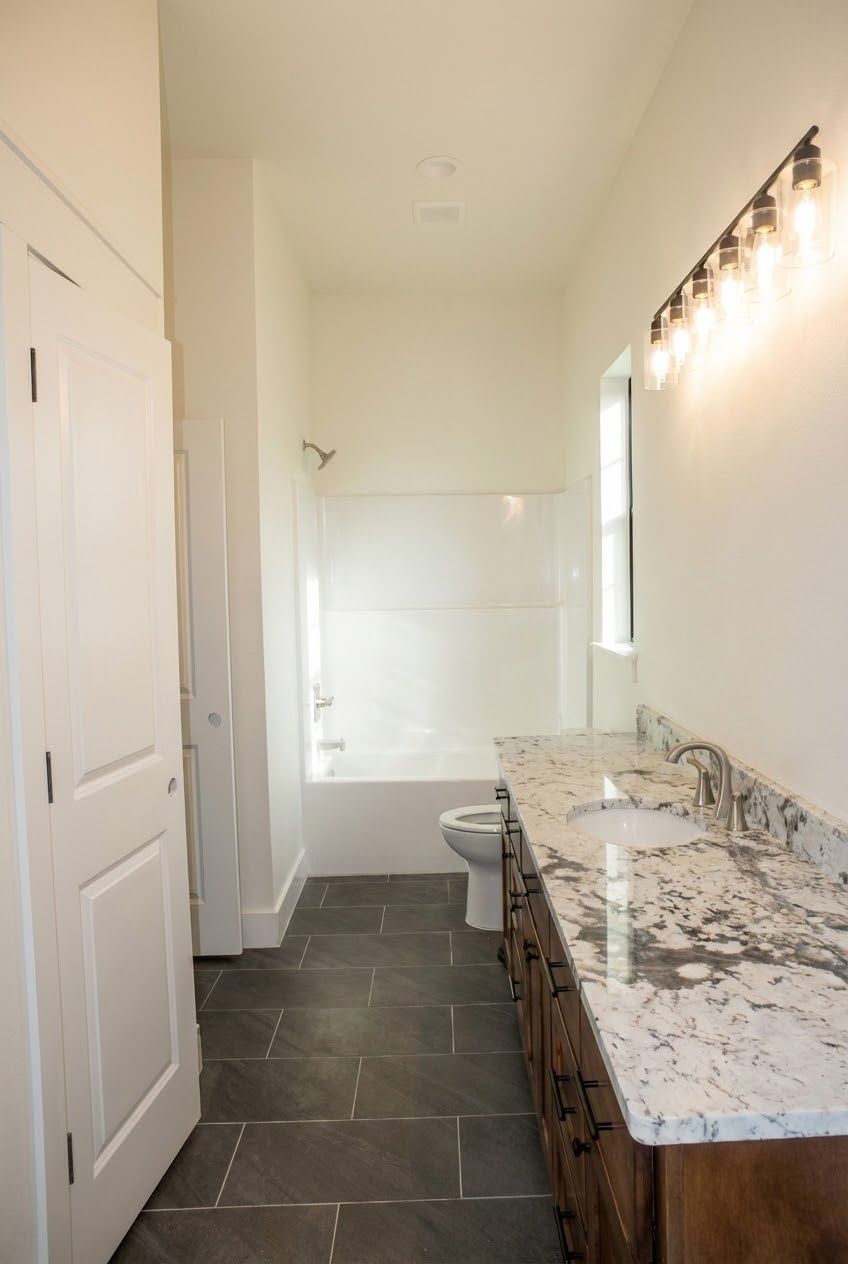 Bathroom with dark gray floor, vanity, toilet, and bathtub. White walls and door.