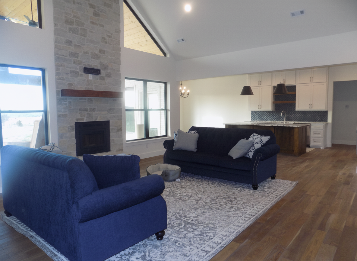 Living room with blue furniture, stone fireplace, and open-plan kitchen.