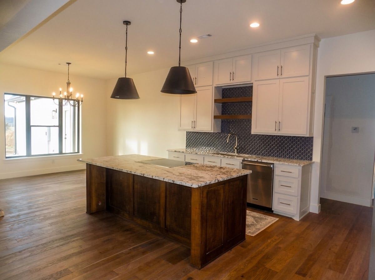Kitchen with white cabinets, dark island, and granite countertops.