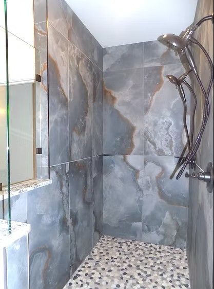 Gray tiled shower with pebble floor, multi-head shower fixture.