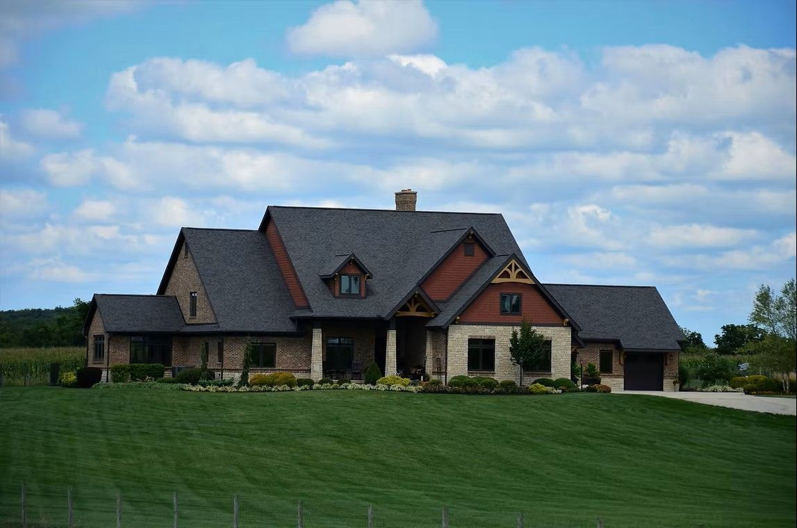 House with stone and red accents, dark roof, and green lawn under a blue sky with clouds.