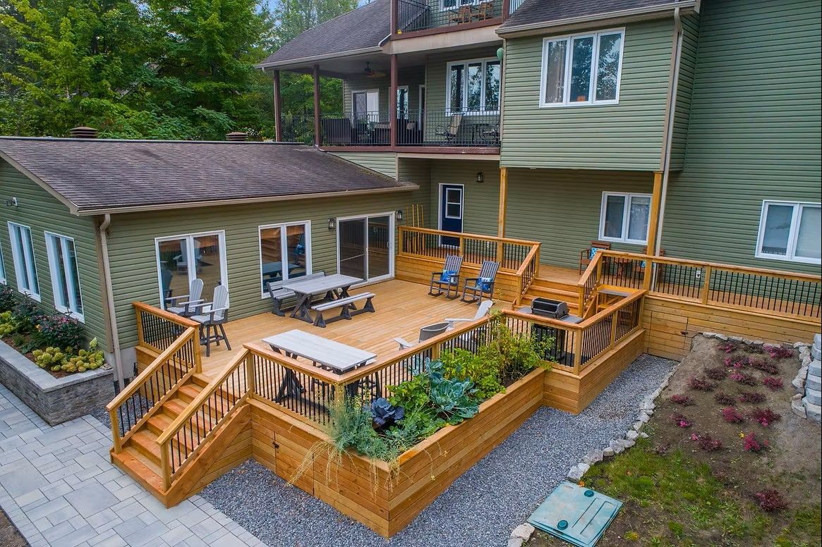 Multi-level wooden deck with green house and foliage.