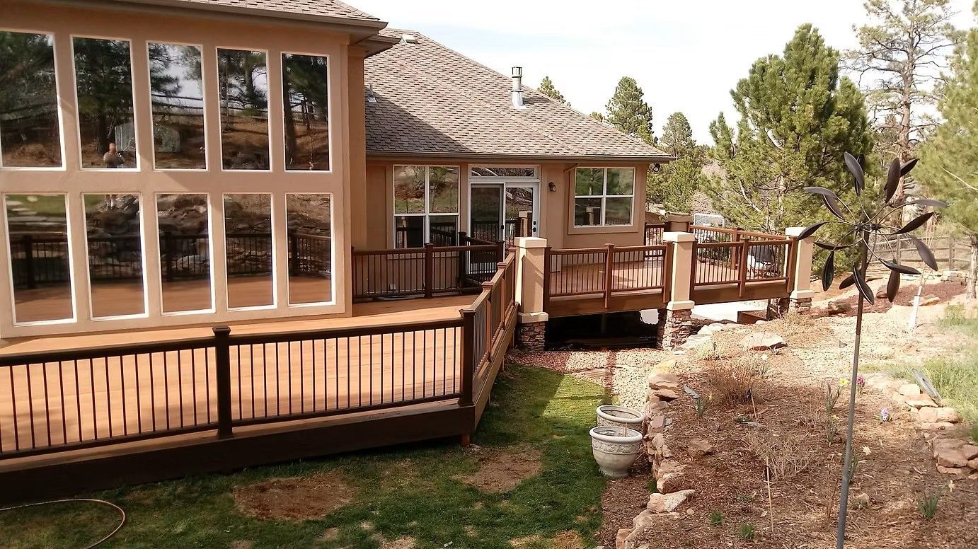 Back of a house with a large deck. Brown wood deck and railing. Large windows. Grassy yard.