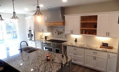 White kitchen with granite countertops, stainless steel appliances, and wood range hood.