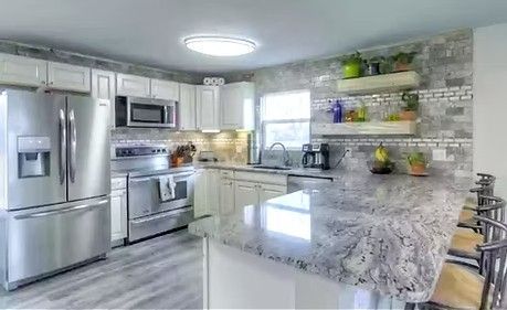 Bright kitchen with white cabinets, stainless steel appliances, and gray granite countertops.