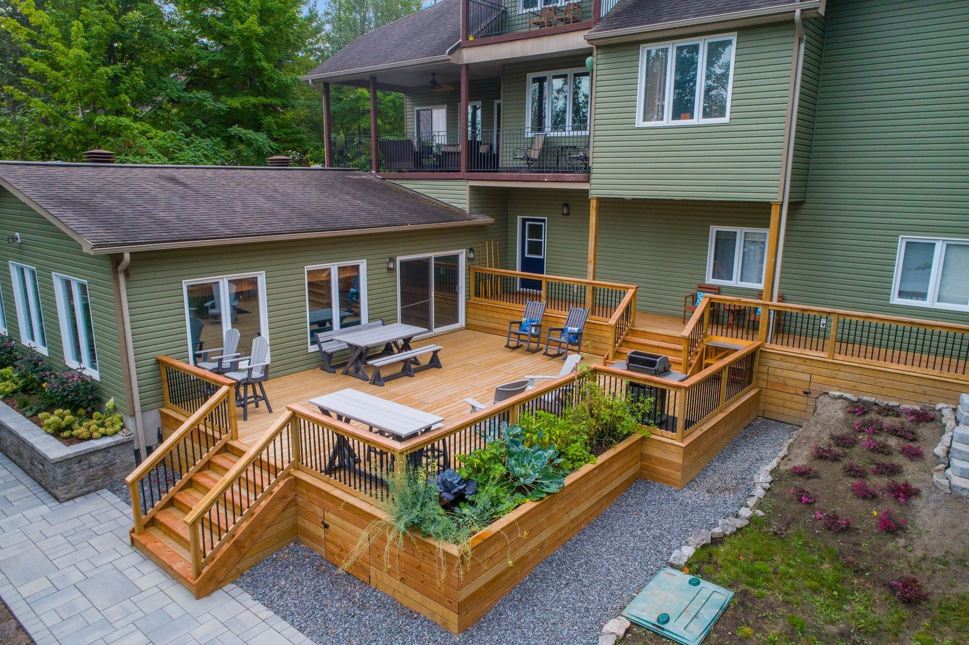 Exterior view of a multi-level house with decks and a gravel garden bed; gray siding, brown deck.