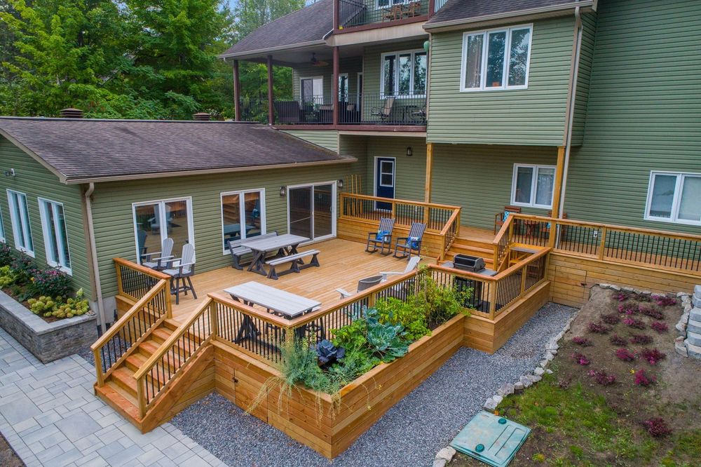 Exterior view of a multi-level house with decks and a gravel garden bed; gray siding, brown deck.