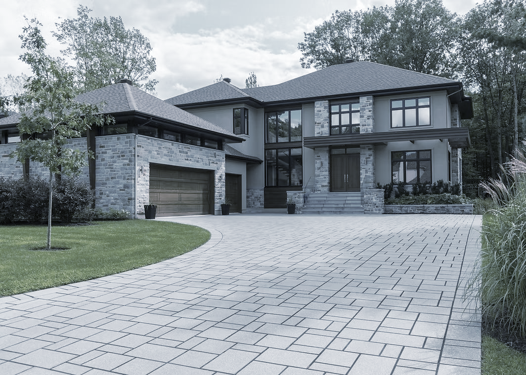 Large modern house with gray stone exterior and patterned driveway.