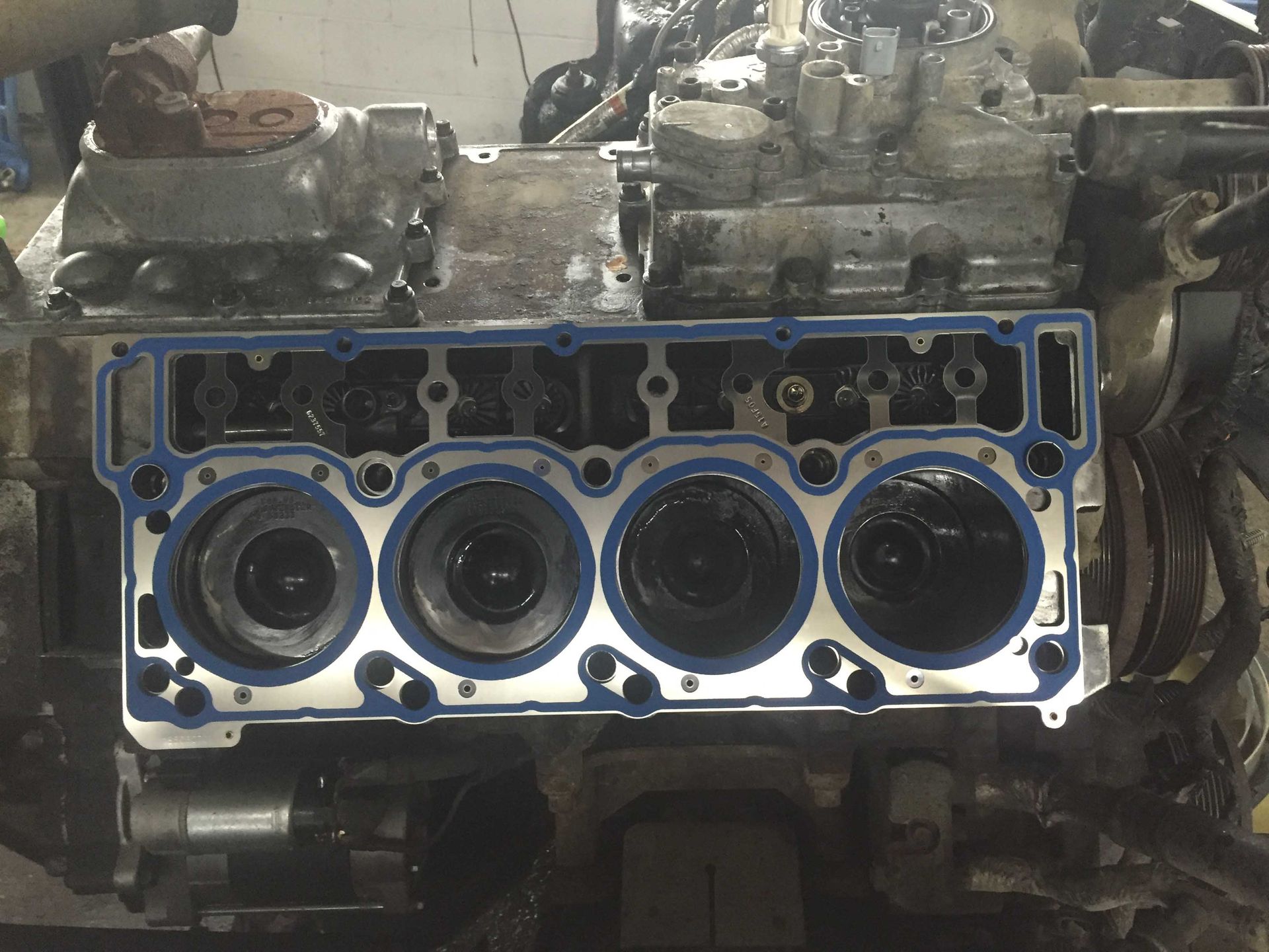 Engine block with gasket in place, cylinders visible. The setting appears to be a repair shop.
