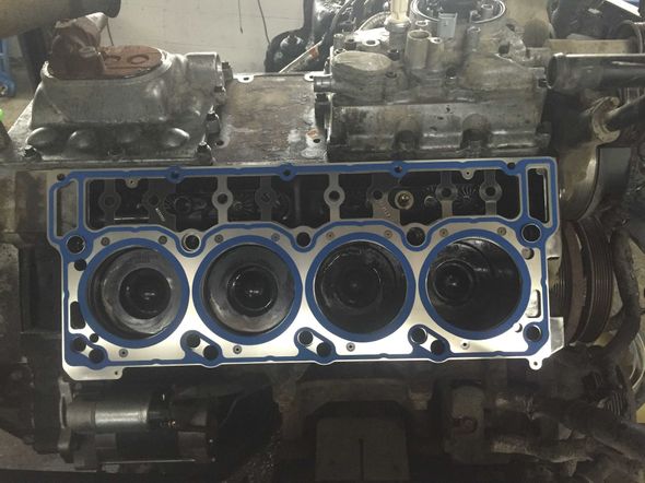 Engine block with gasket in place, cylinders visible. The setting appears to be a repair shop.