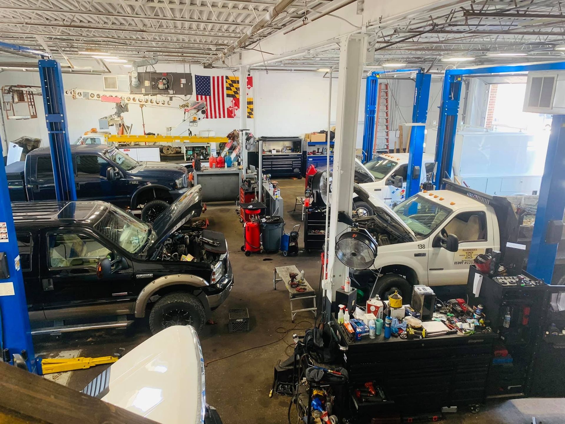 Interior of an auto repair shop with multiple pickup trucks on lifts. Tools and equipment are visible.