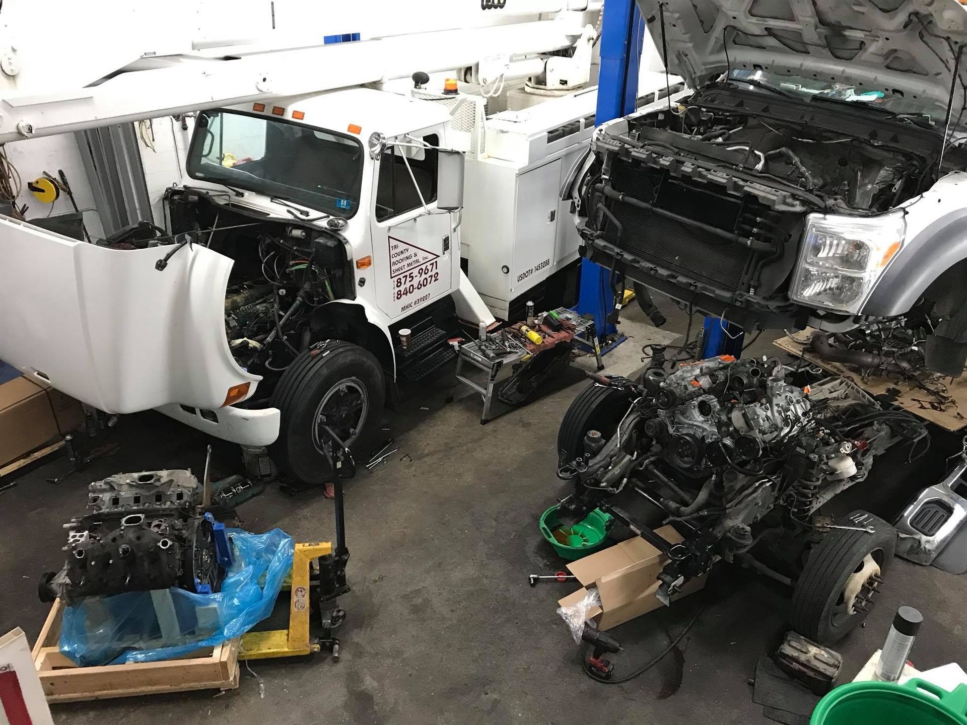 Two white trucks disassembled in a repair shop; parts scattered on the floor.