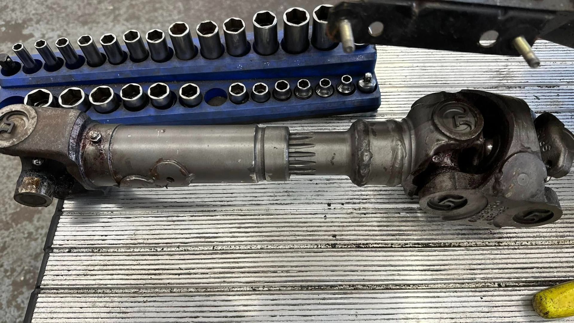 Driveshaft with universal joints, sockets, and tools on a work surface.