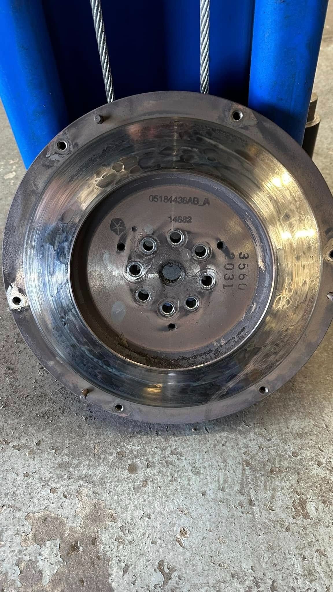 A worn, circular flywheel with bolt holes, against a blurry blue background.