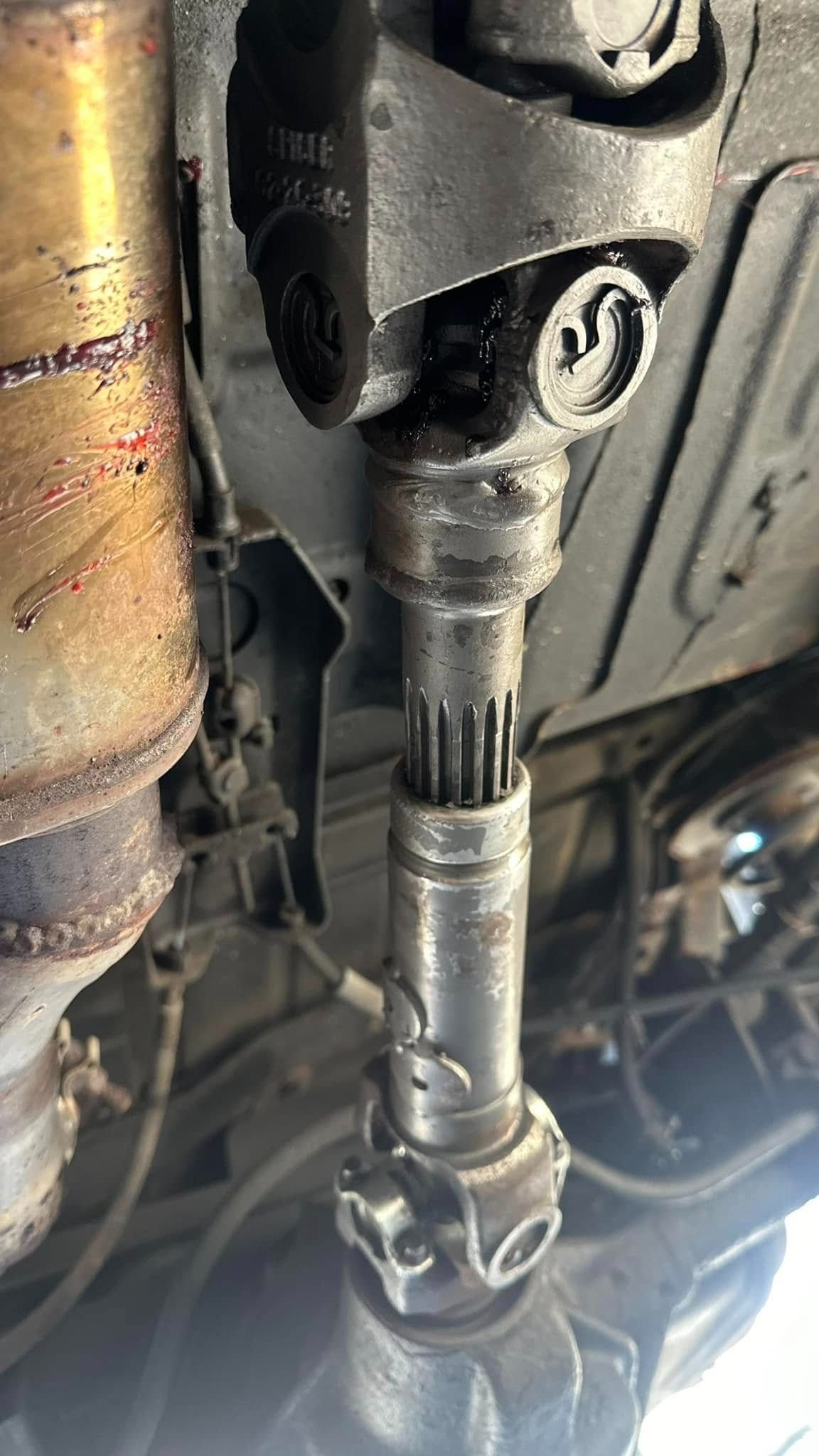 Drive shaft of a vehicle, seen from underneath. Gray metal components, greasy.