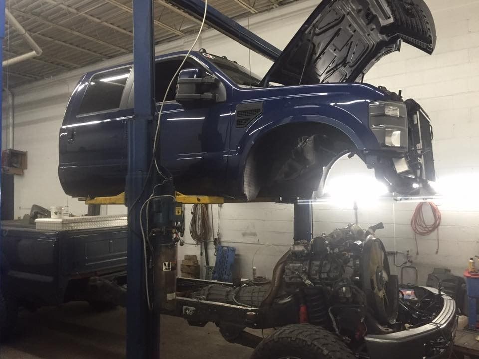 Blue truck cab lifted above the chassis in a shop with open hood, undergoing repair.